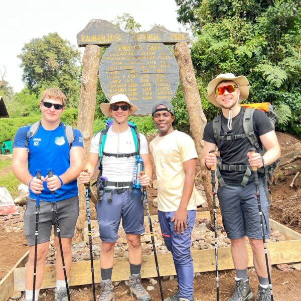 Four hikers with backpacks and trekking poles pose in front of the Kilimanjaro National Park via Lemosho route